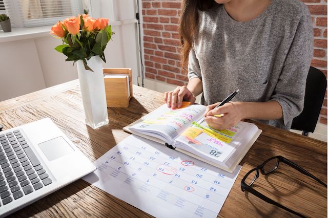 A woman organizes her schedule at work by writing appointments in her daily planner 