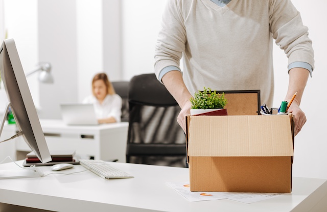 A male employee stands by his desk with his belongings in a box