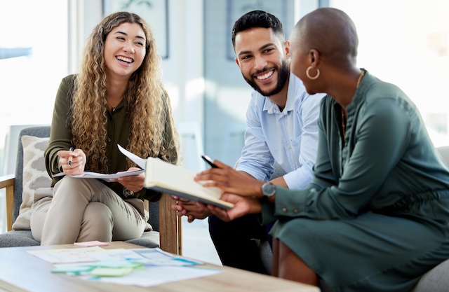 Three colleagues, two women and one man, sit in a casual setting, happily meeting on a work project